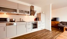 Wohnzimmer mit offener Küche und Zugang zum Balkon